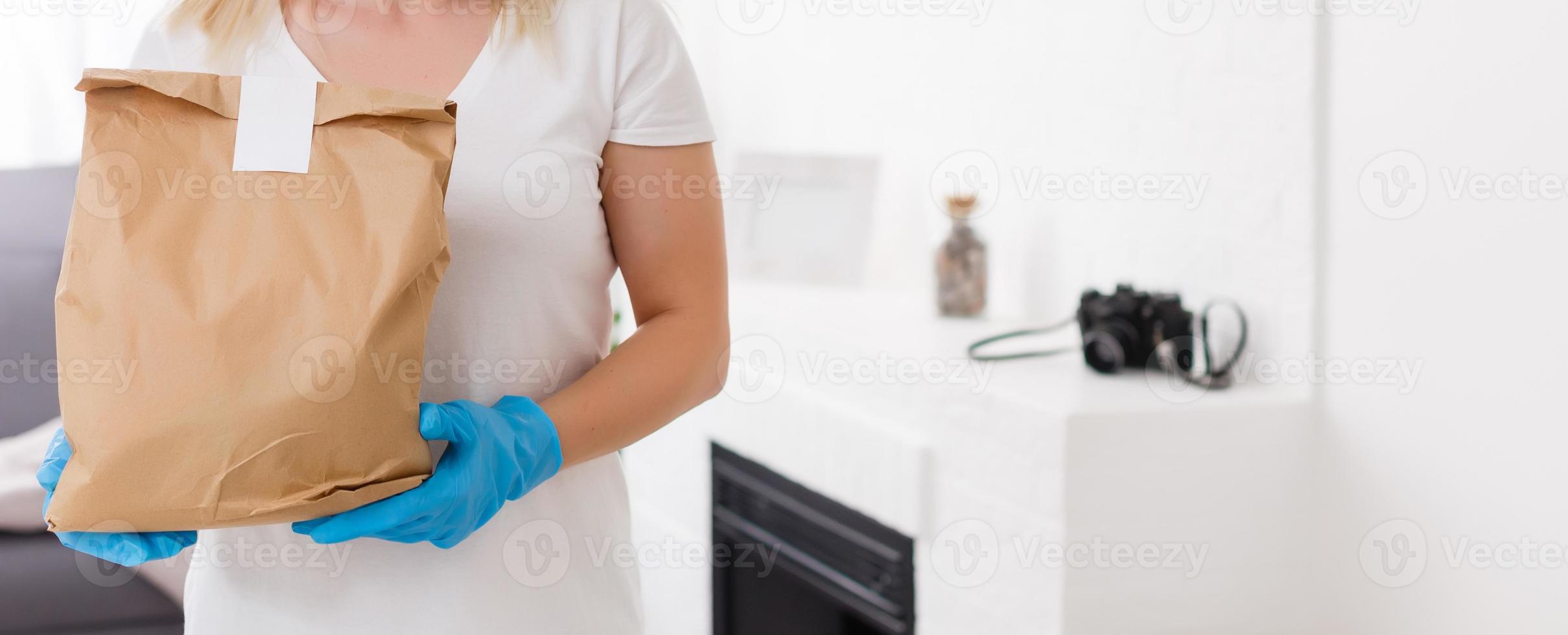 Young woman wearing medical mask receiving parcel from delivery indoors. Prevention of virus spread photo