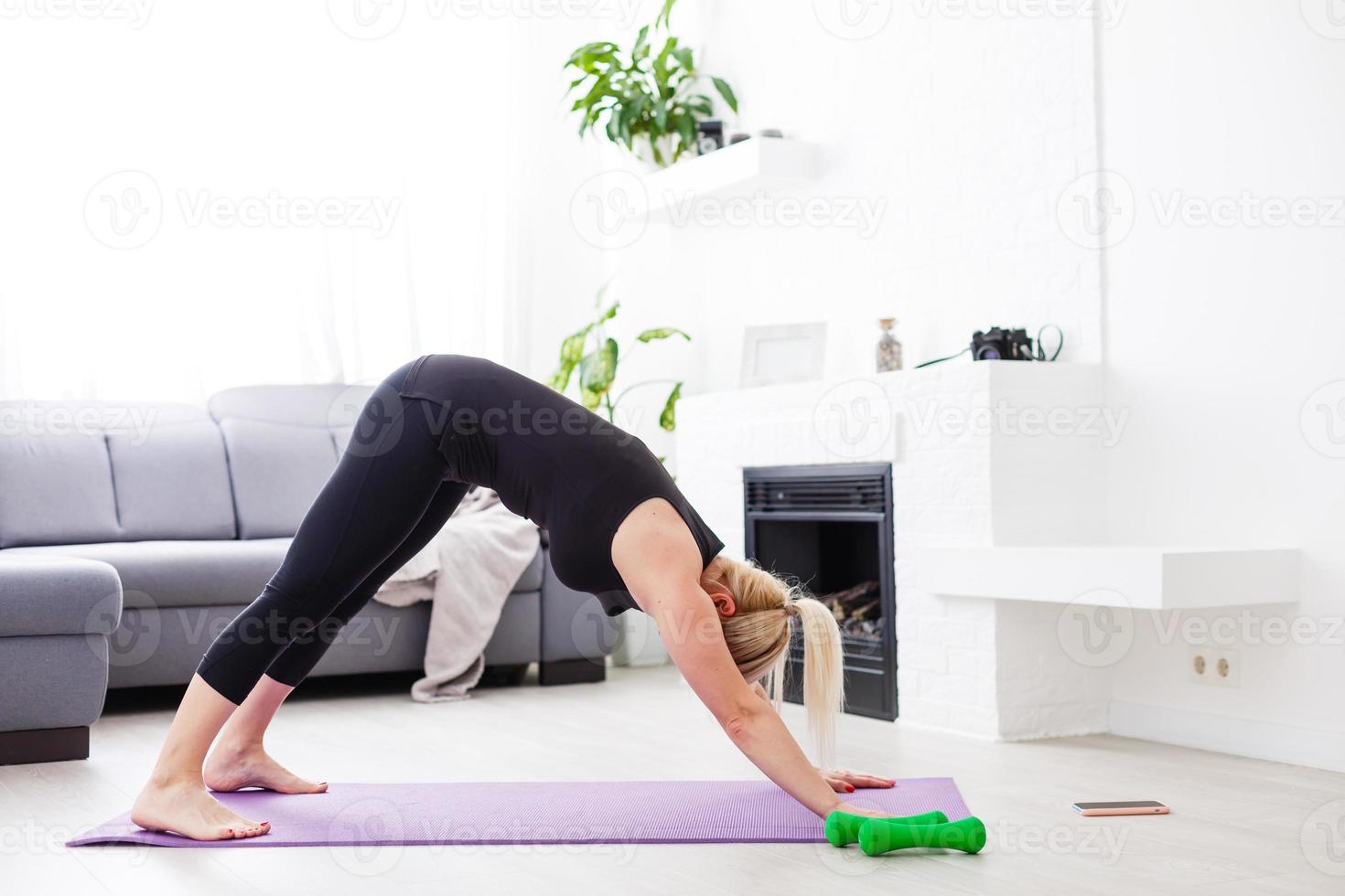 un Delgado europeo niña haciendo extensión ejercicios a hogar en un yoga estera, rayos de ligero brillar desde el ventana. llamarada. cuarentena deporte. foto