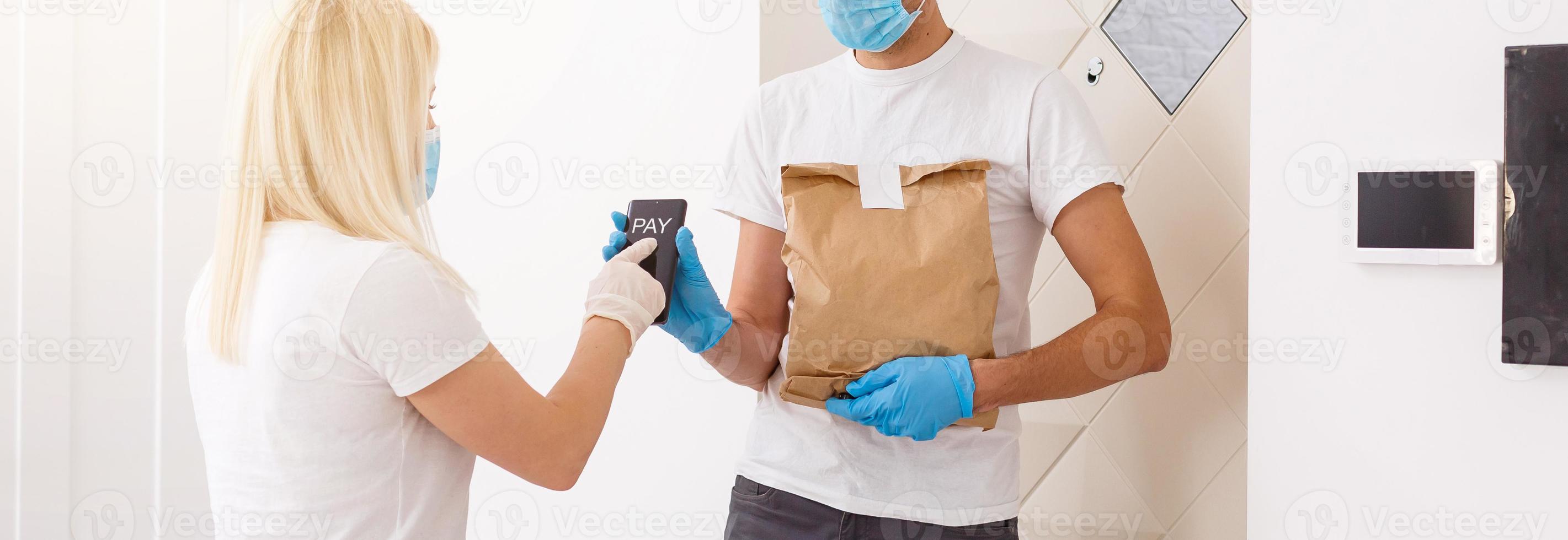 Courier in protective mask delivers parcel, customer in medical gloves receives box. Delivery service under quarantine, disease outbreak, coronavirus covid-19 pandemic conditions. photo