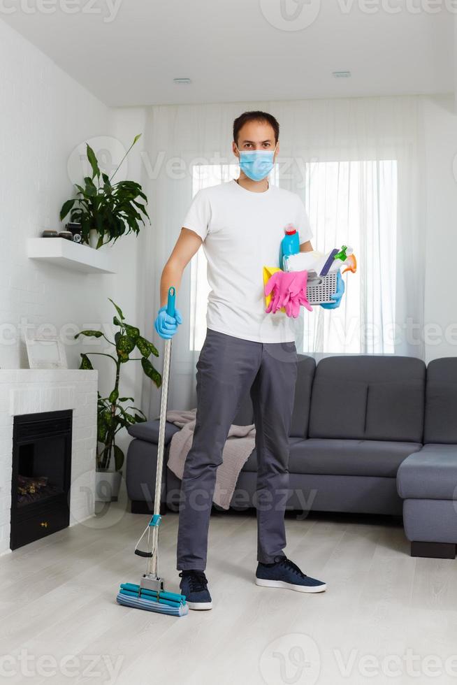 cleaning, health and hygiene concept - indian man wearing protective medical mask for protection from virus disease in gloves with detergent and mop at home photo