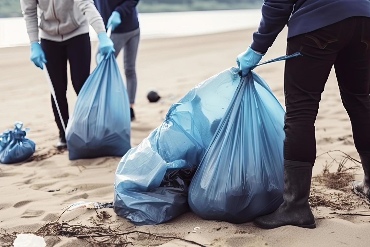 a group of unrecognizable people collecting garbage from the beach in blue bags for the problem of plastic pollution in the environment photo