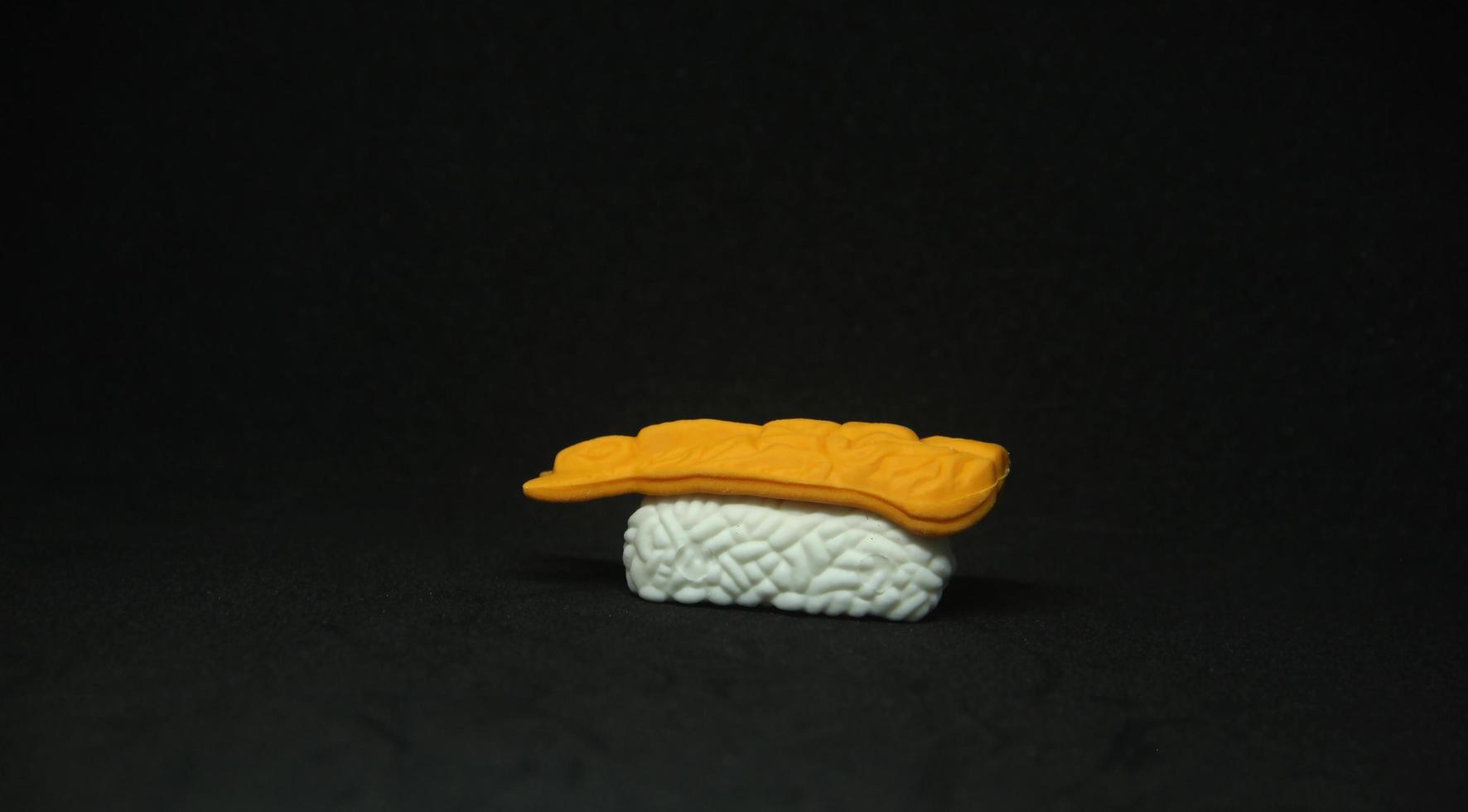 Japanese food sushi small eraser toy miniature stationary with unique cute shape. Sushi with rice and fish on top isolated photo on dark black background.