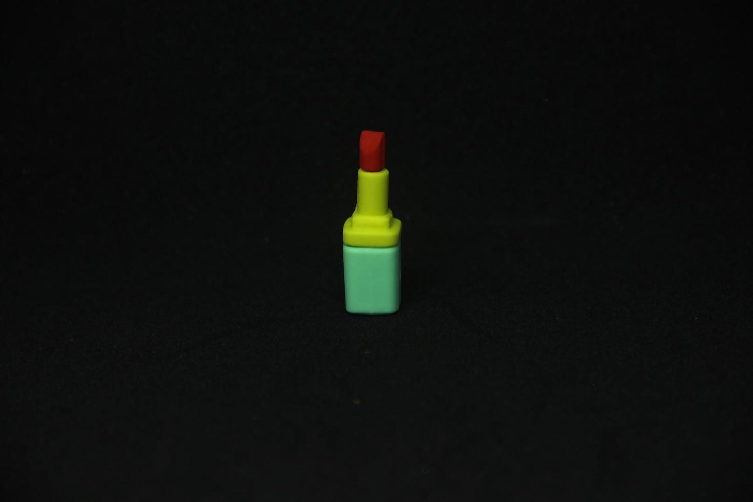 Red lipstick with yellow and green container tube shaped eraser stationary tools for office or school supplies. Isolated photo on plain dark black background.