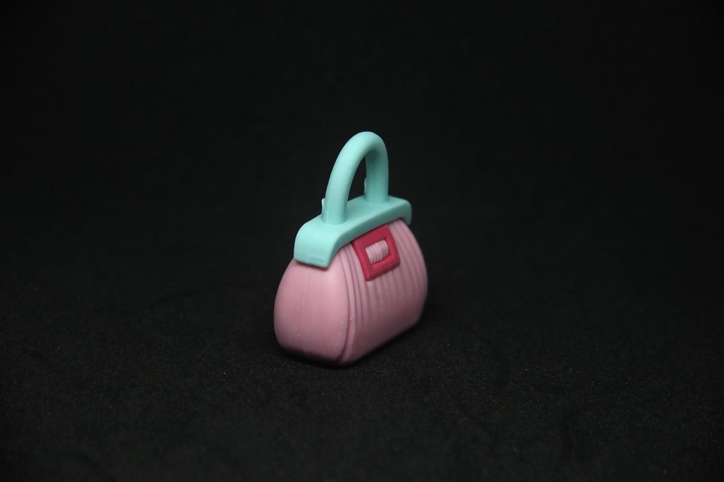 Pink women bag with blue handle shaped eraser stationary tools for office or school supplies. Isolated photo on plain dark black background.