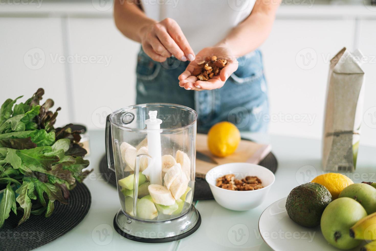 Young slim woman in white t-shirt and blue jeans cooking smoothie with bananas healthy food in kitchen at home photo