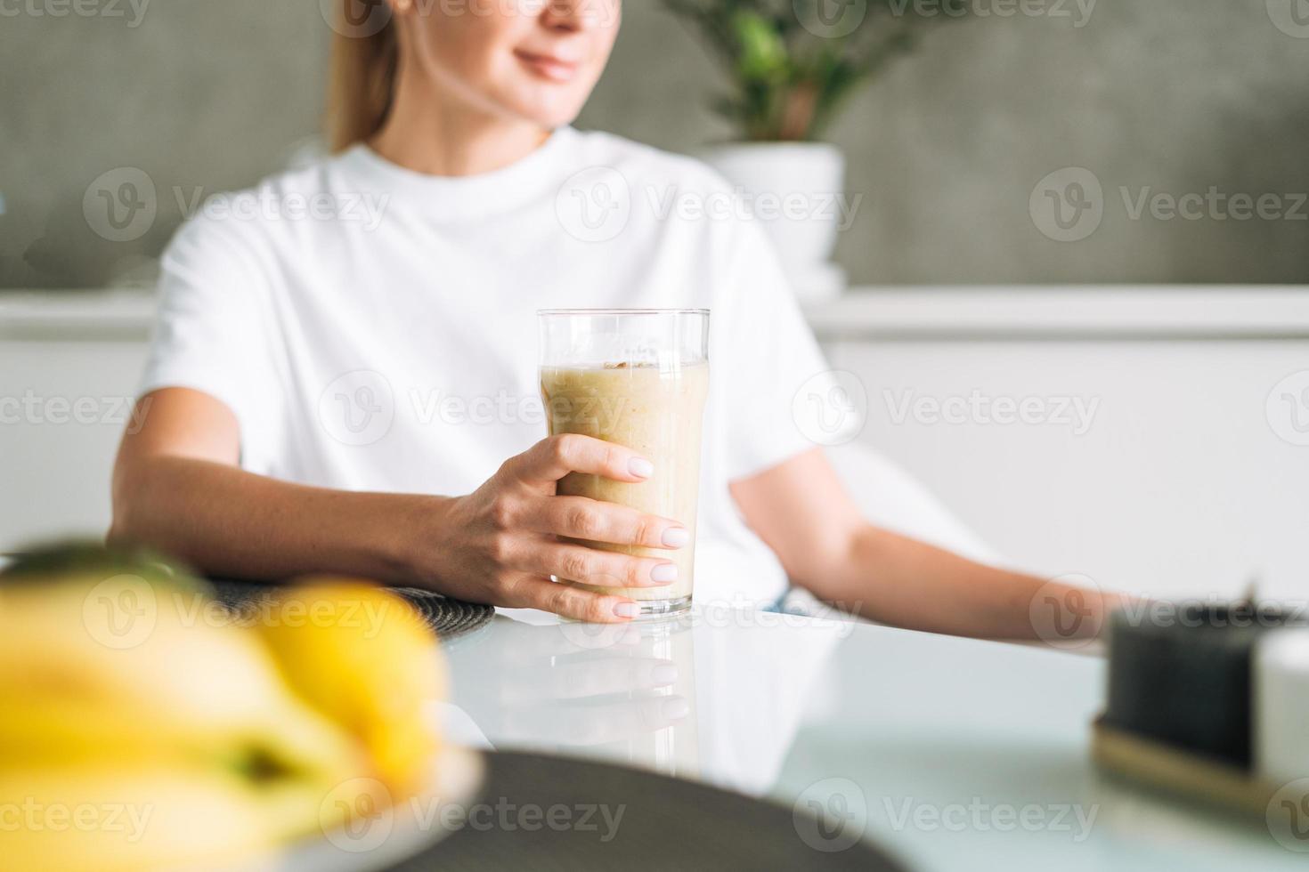 Young slim woman in white t-shirt and blue jeans drinking fruit smoothie healthy food in kitchen at home photo