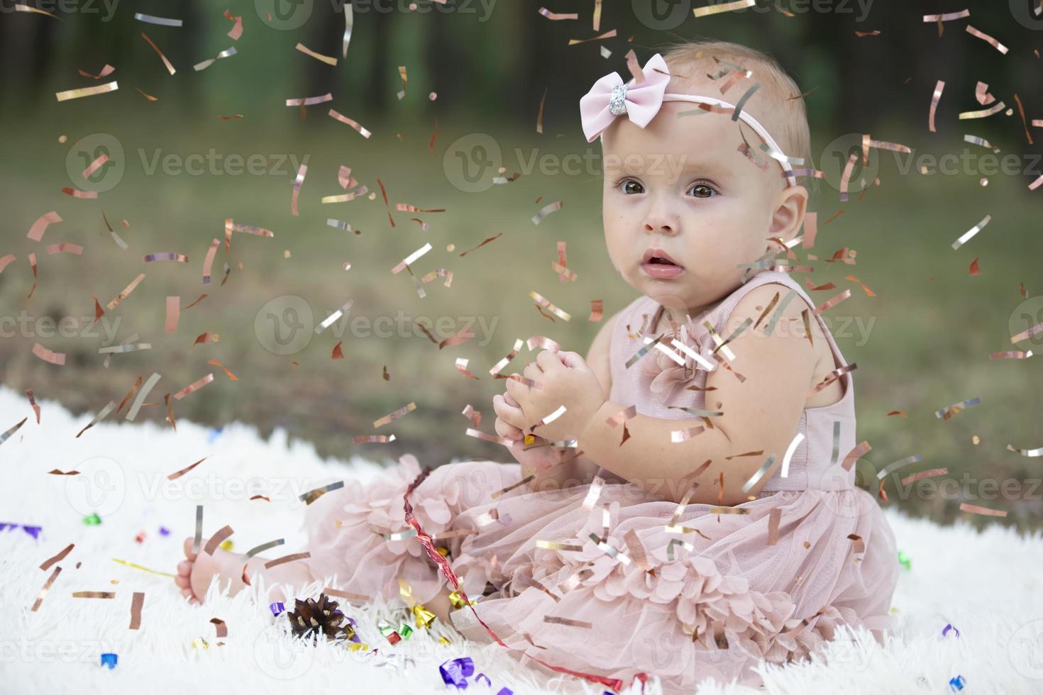 A funny little girl in a bright confetti. Child celebrates one year. Beautiful baby. photo