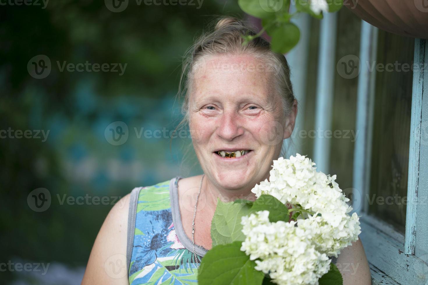 Portrait of a cheerful old woman with gold teeth and white flowers. photo