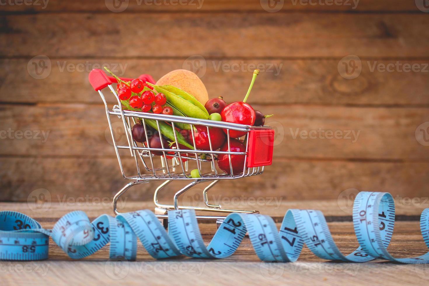 Shopping cart with fruits, berries and tape line on old wood background. Toned image. photo
