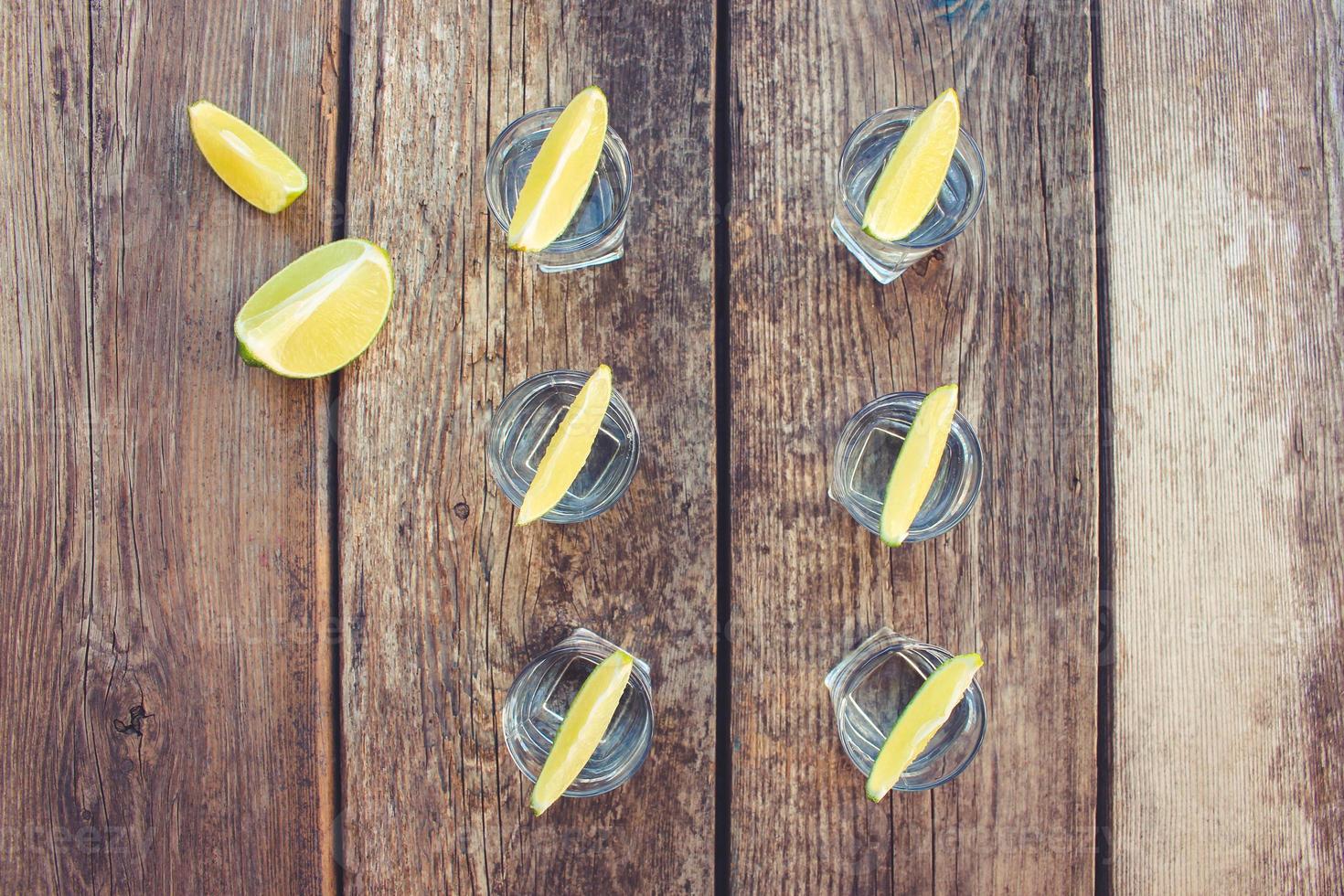 Vodka and lime slices on wooden background. Toned image. Top view. photo