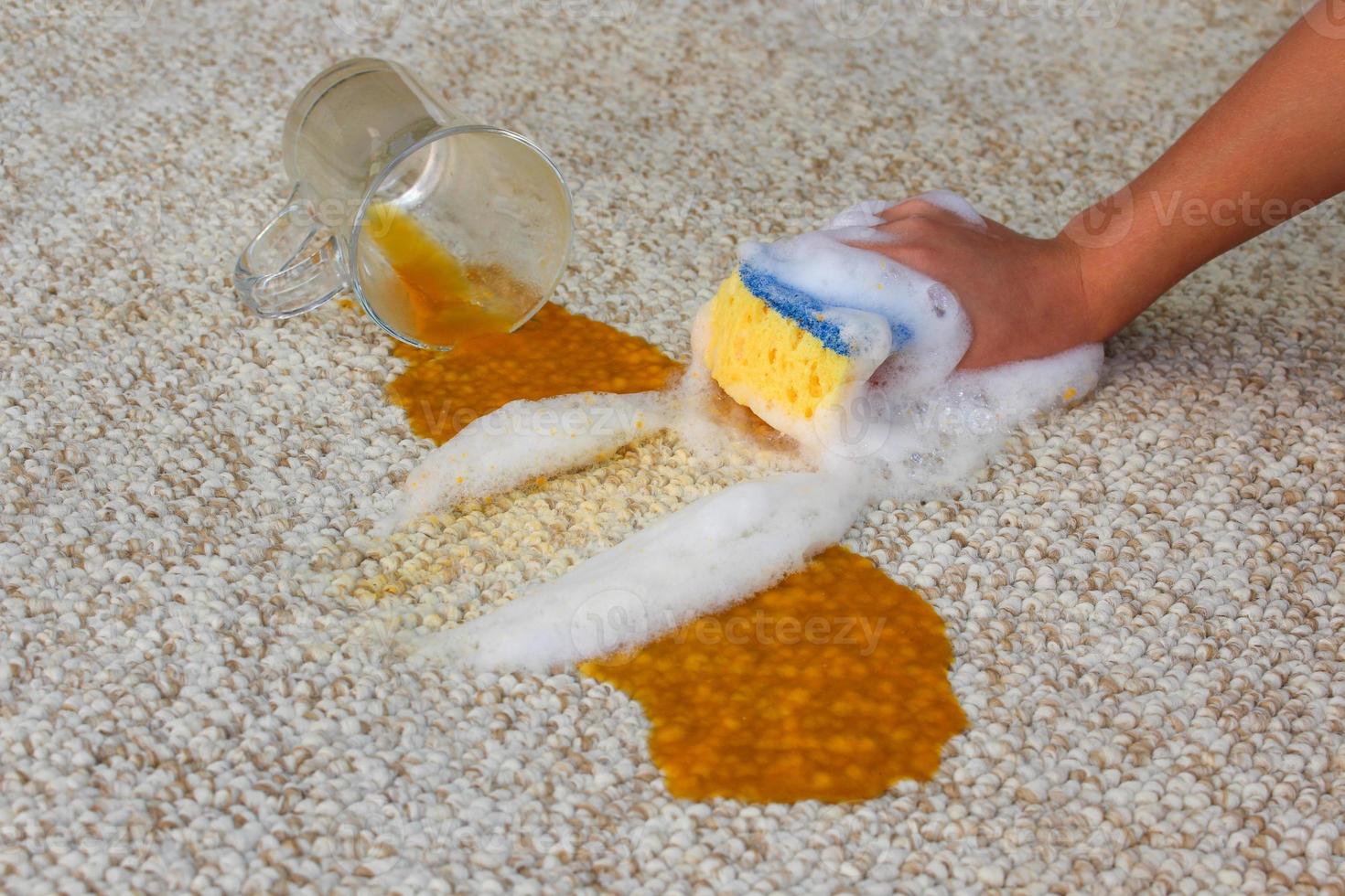 Glass of juice fell and spilled on floor. Female hand cleans the carpet with a sponge and detergent. photo