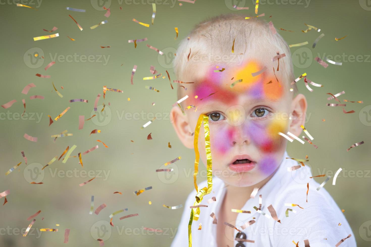 A funny little boy with a face smeared with paints looks at the flying confetti. The child is at the party. photo
