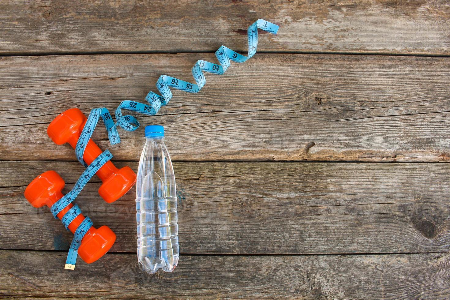 Dumbbells, water, measure tape on old wooden background. Top view. photo