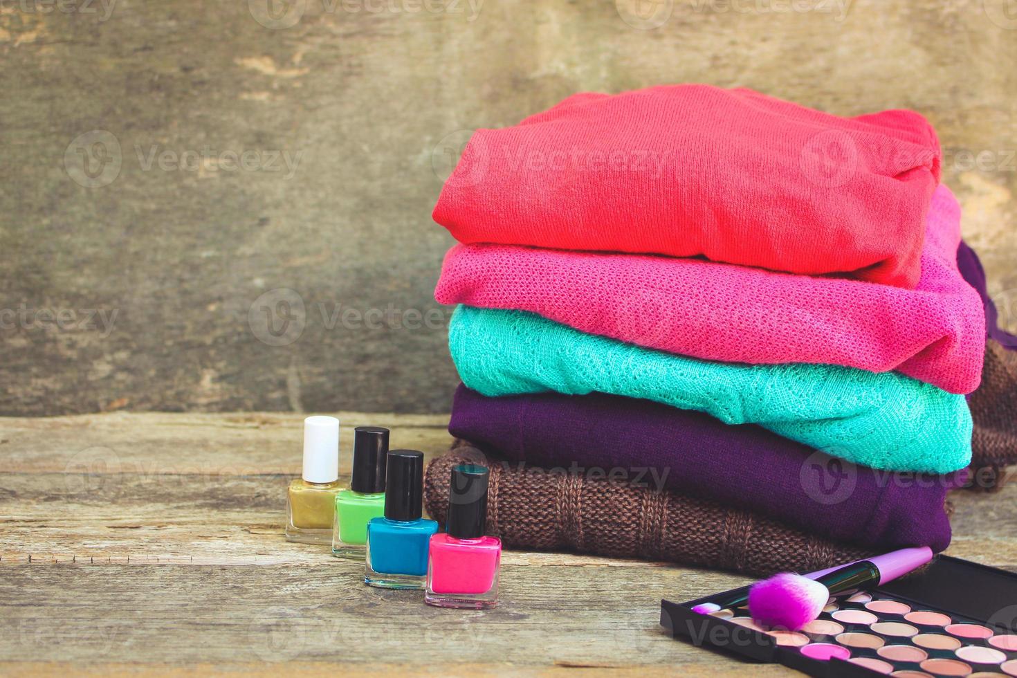 Women's clothing and cosmetics sweaters, nail polish, eye shadow, brushes on wooden background. Toned image. photo