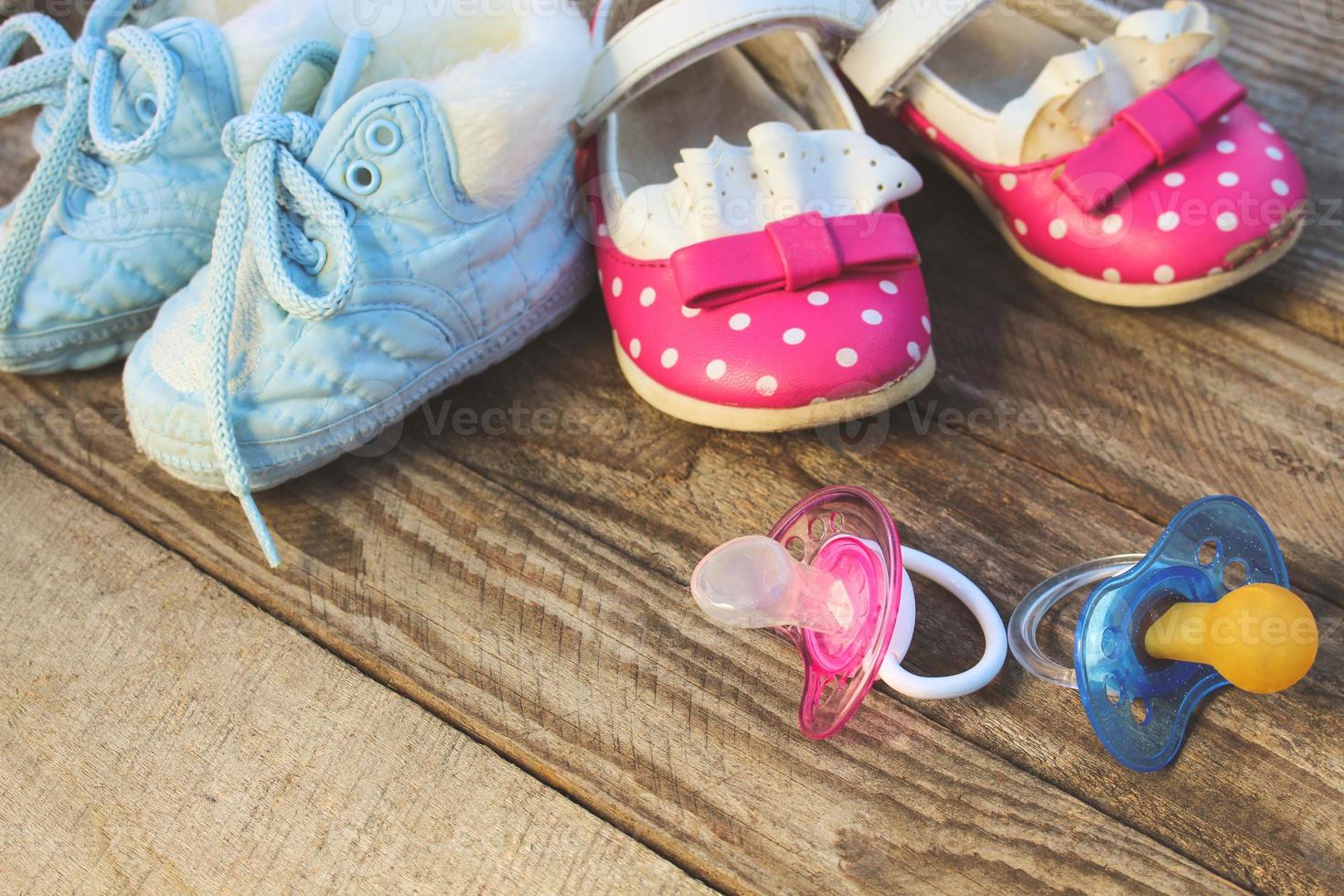 Baby shoes and pacifiers pink and blue on the old wooden background. Toned image. photo