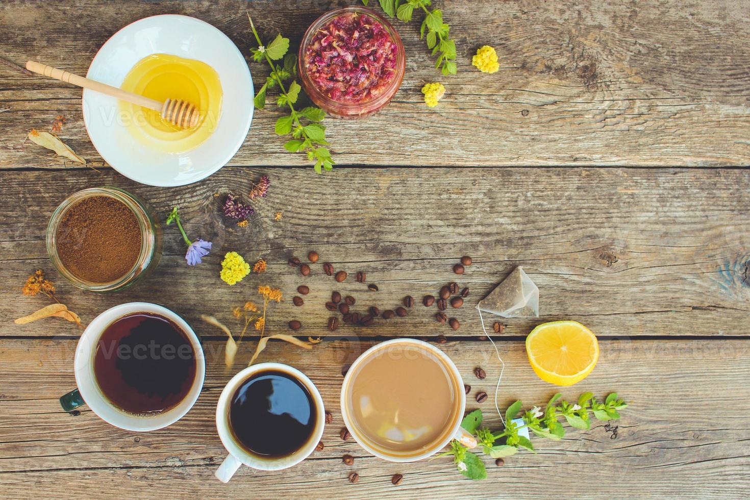 Tea, coffee, cocoa in cups, chicory, lemon, mint, jam made of rose petals, dried lime, honey on the old wooden background. Toned image. Top view. photo