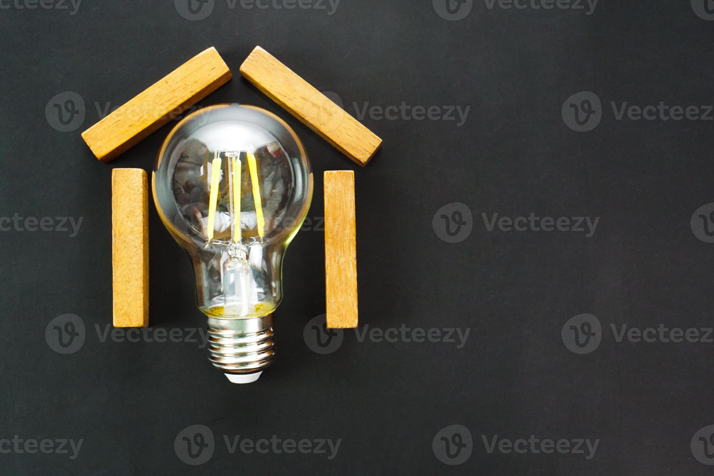 House shaped wooden block with light bulb inside on black background