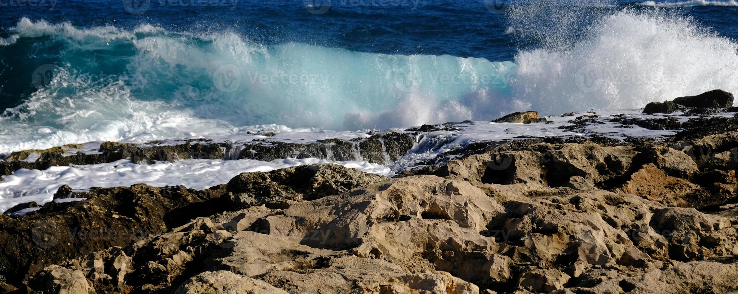 Blue sea wave and white foam and splash. Stone beach on island of Malta, no sandy beach. Summer holiday border frame concept. Tropical island vacation backdrop. Tourist travel banner design template. photo