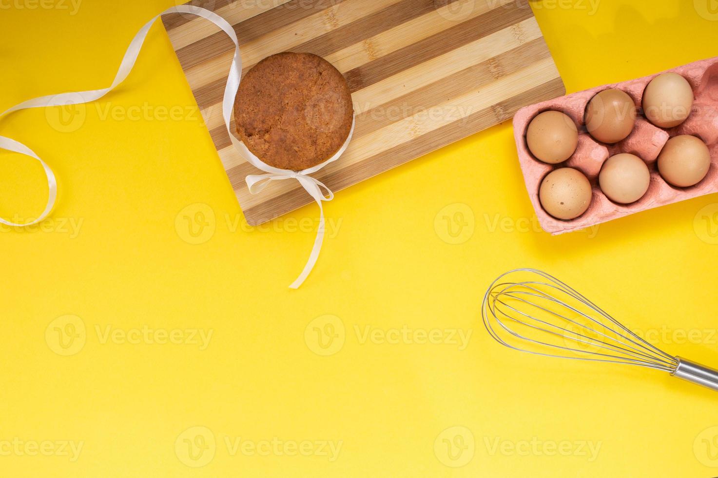Easter pastries on the table with chicken eggs and a whisk on a yellow background. Top view photo
