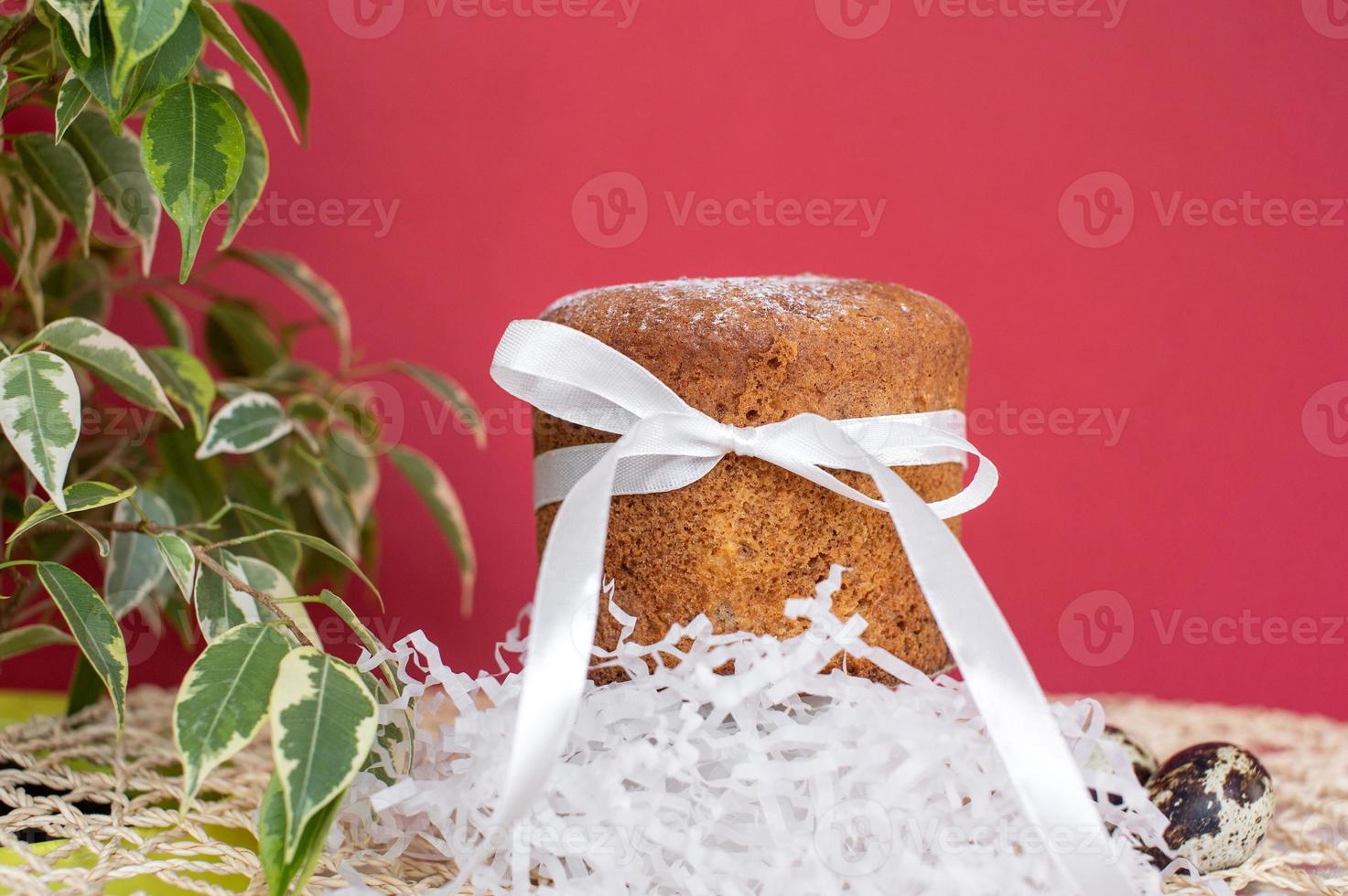 Sponge Easter cake with a white ribbon with quail eggs on a red background with a green plant. photo