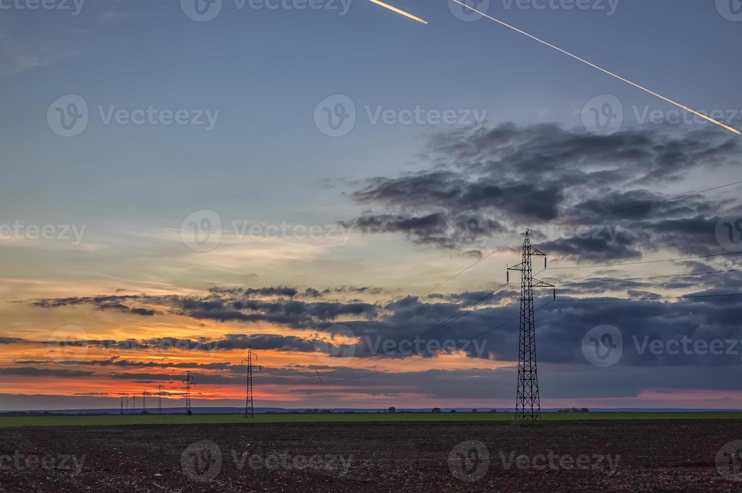 Poles and overhead power lines silhouettes in the dusk. Electricity generation and distribution. Electric power industry and nature concept photo