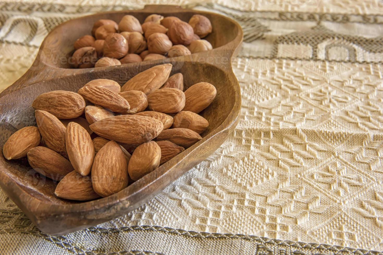 Almendras y avellanas en el de madera cuenco en el mesa, de cerca foto