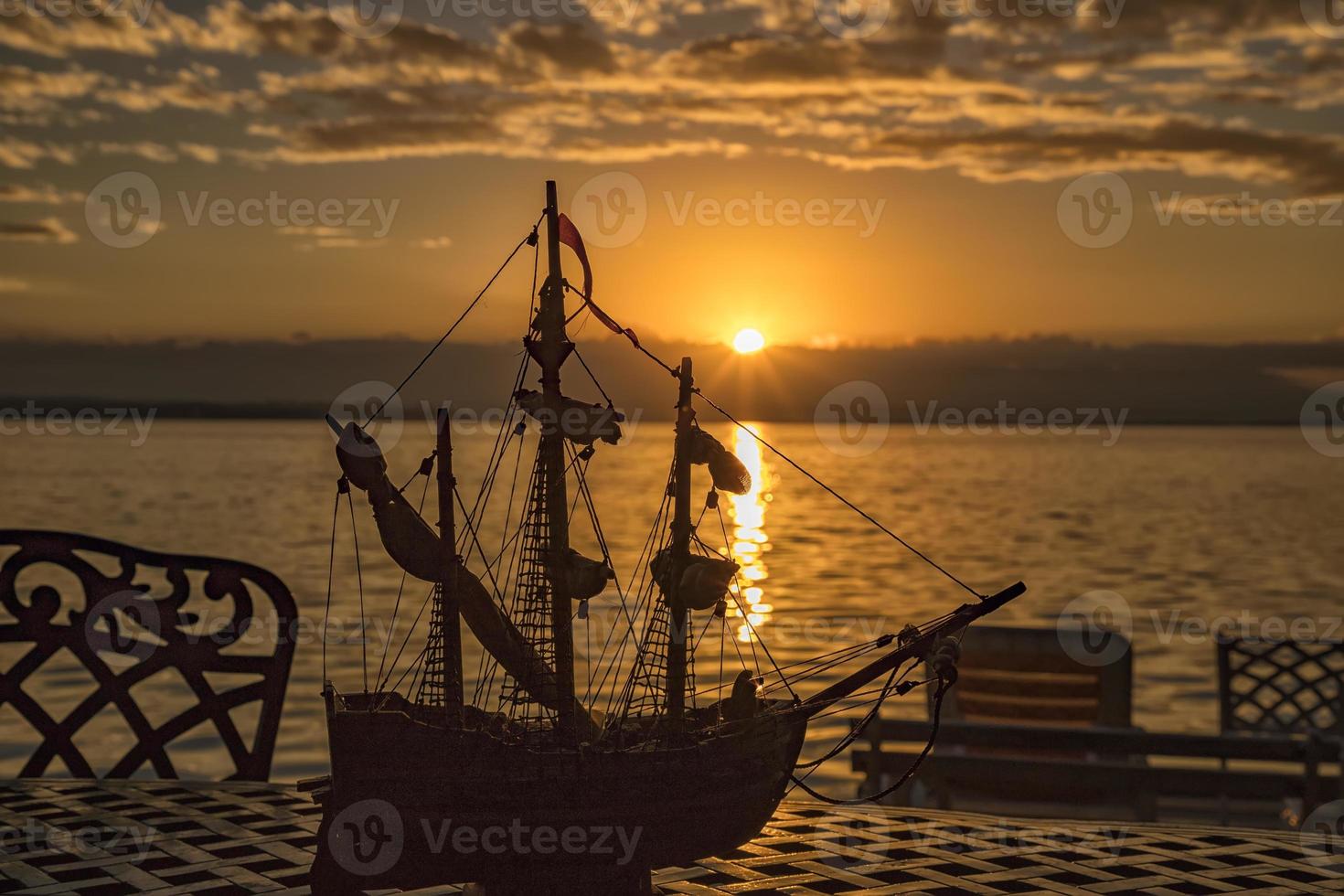 A silhouette of a chair and ship toy on a table at sunrise at the sea beach photo