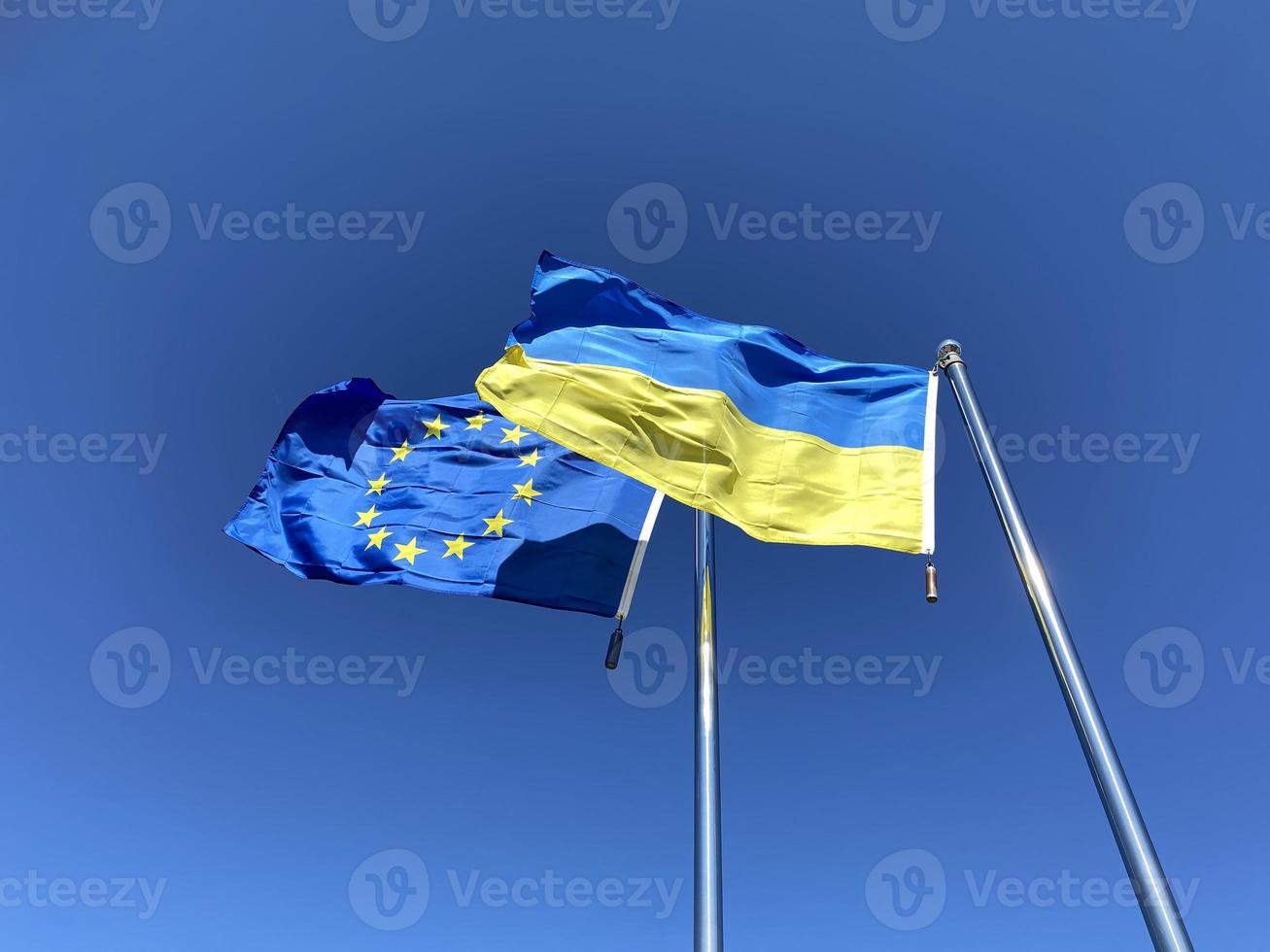 Ukrainian and European Union flags on flagpoles against blue sky photo