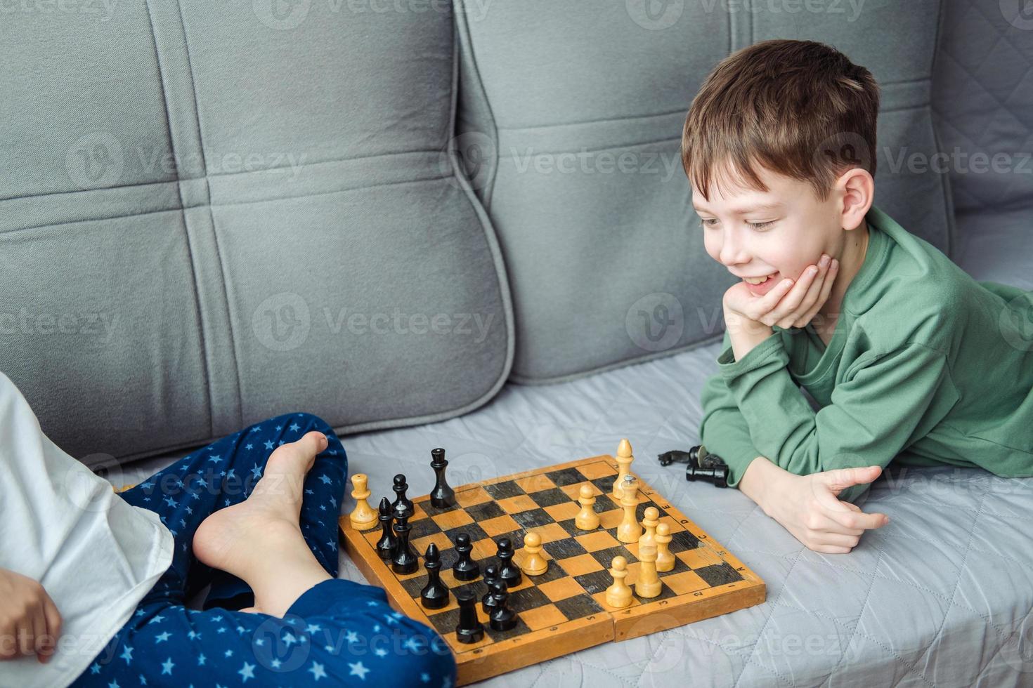 Niños jugar de madera ajedrez acostado en un gris sofá. foto