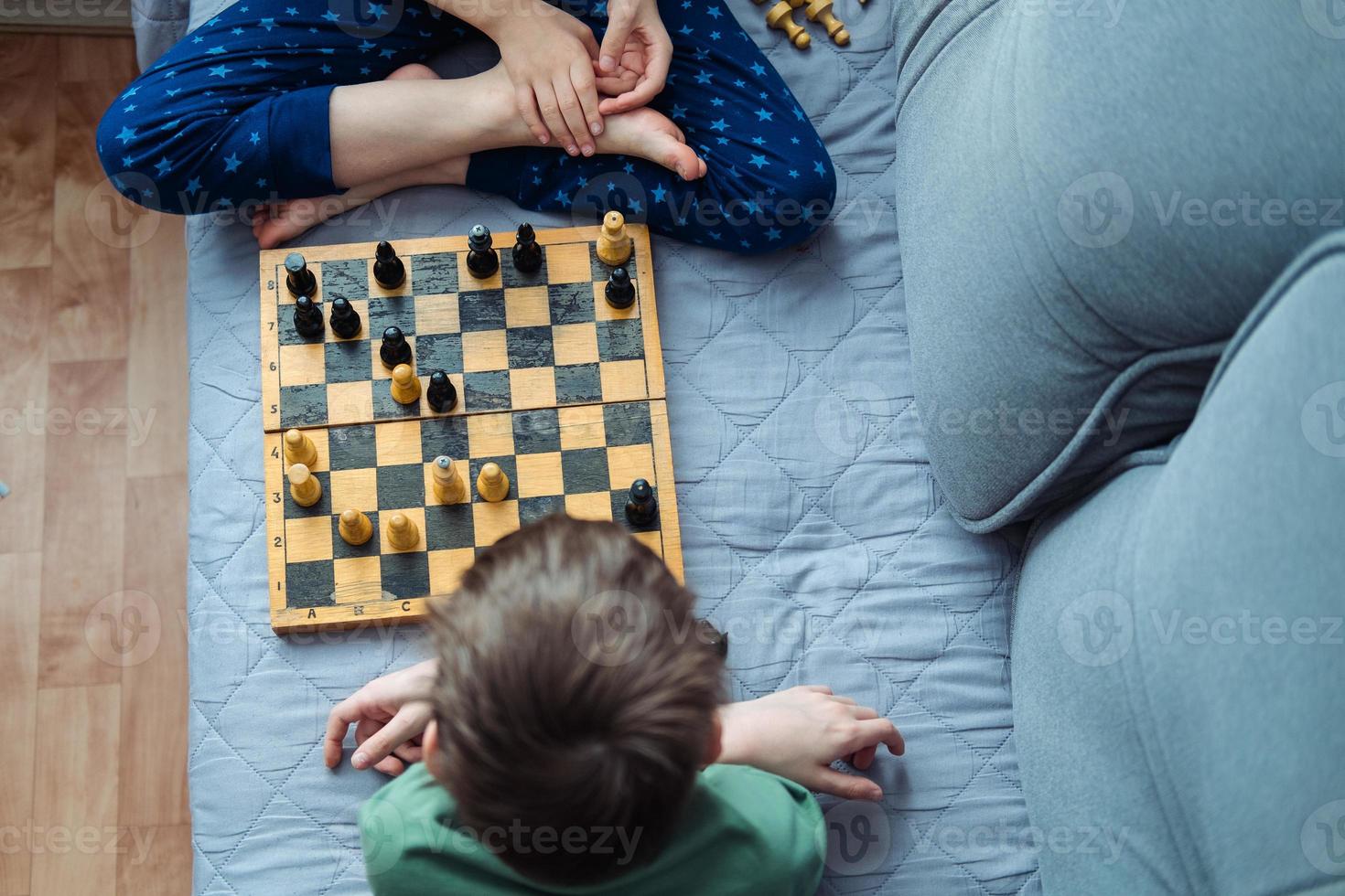 Boys playing wooden chess lying on a gray sofa, top view photo
