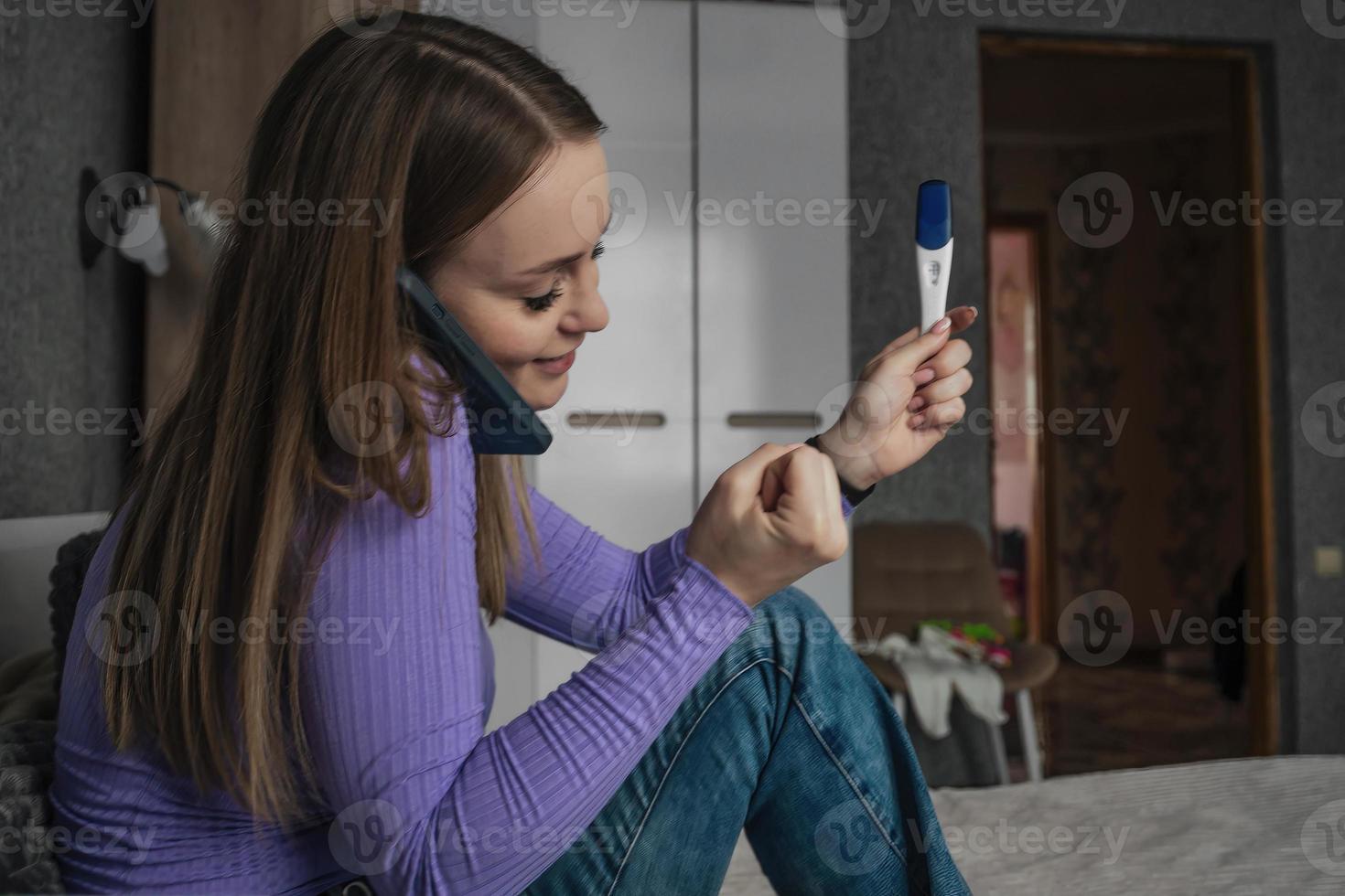 a young beautiful woman rejoices and is happy, in her hands a positive pregnancy test, she shares her joy on the phone photo