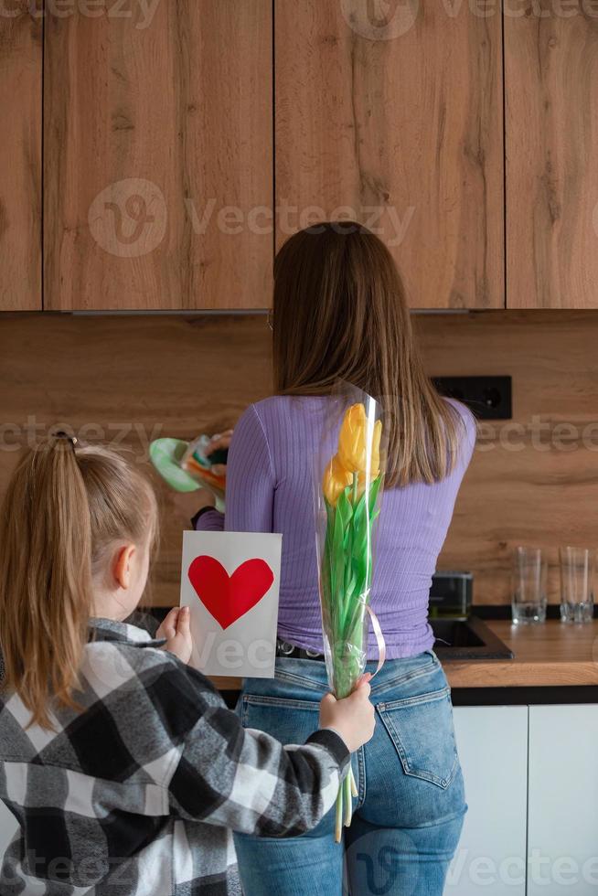 Daughter congratulates mom on Mother's Day, card with heart and flowers. A woman washes dishes and is busy with household chores. photo