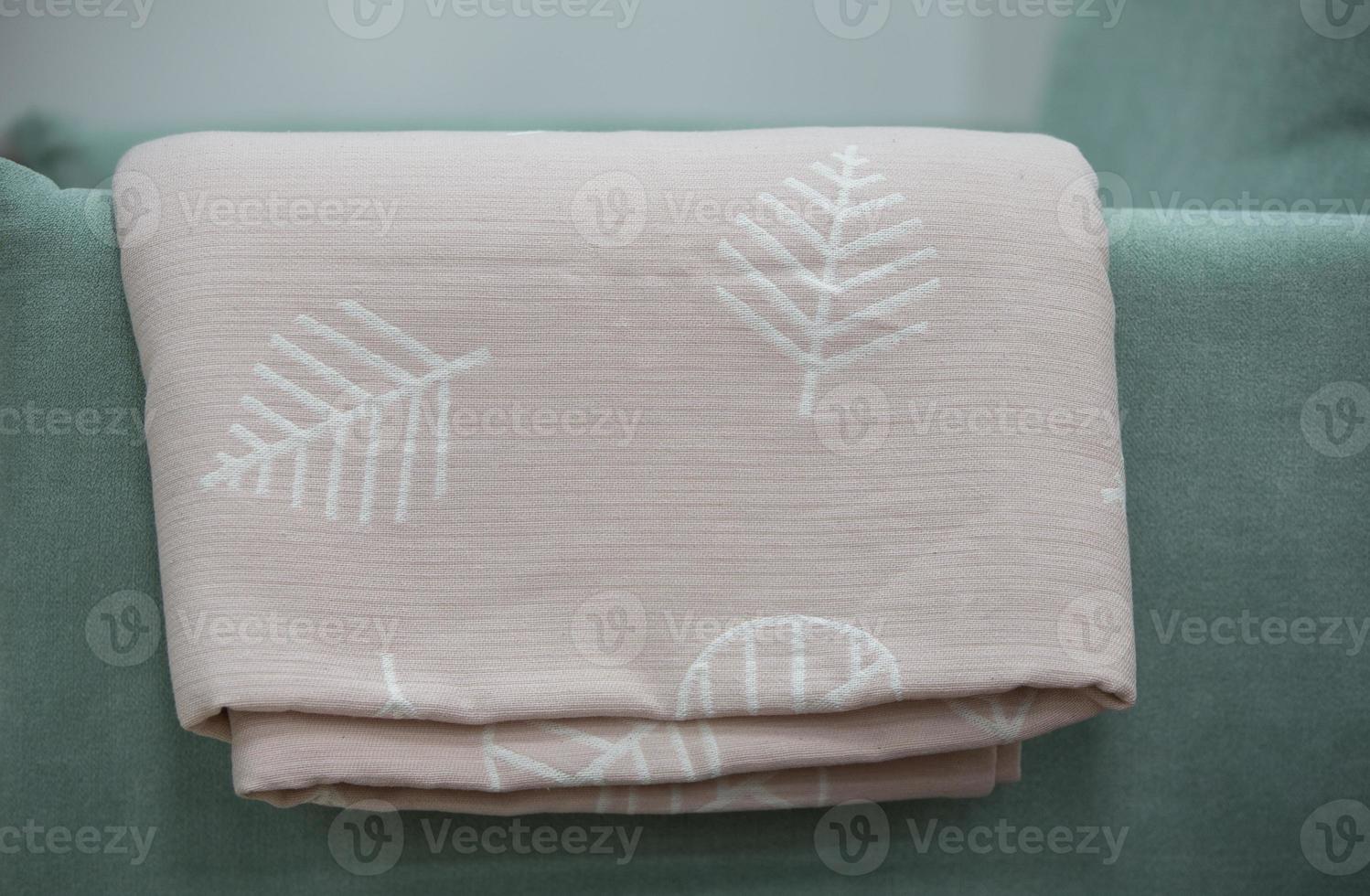 A pink coverlet with a floral motif rests on the green back of the sofa. photo