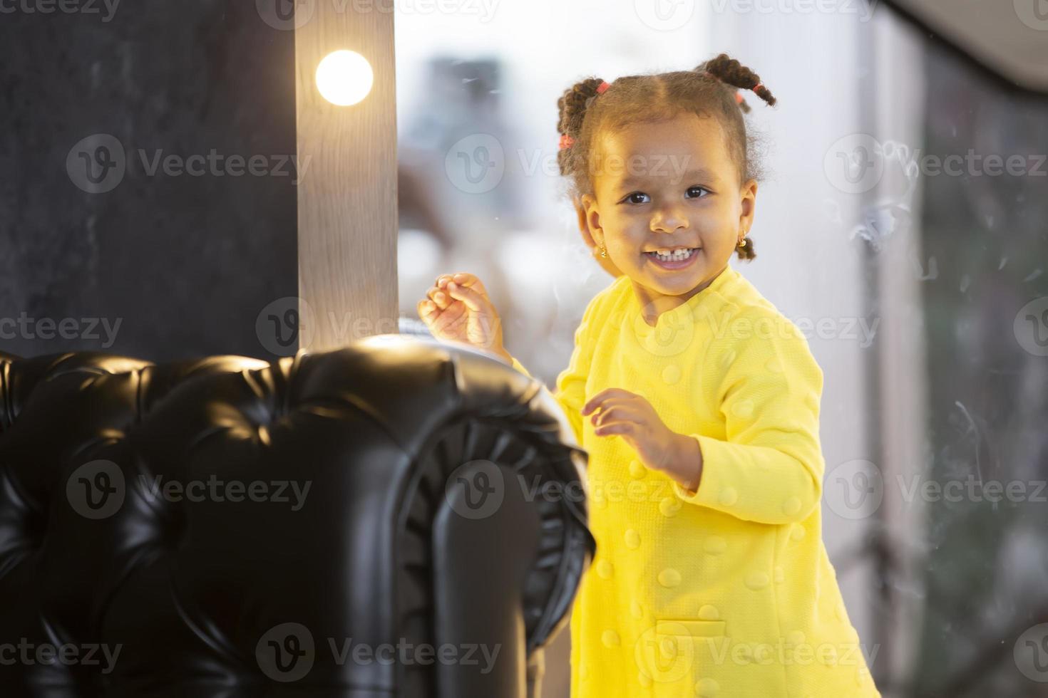 A little African American girl stands near the mirror and smiles. photo