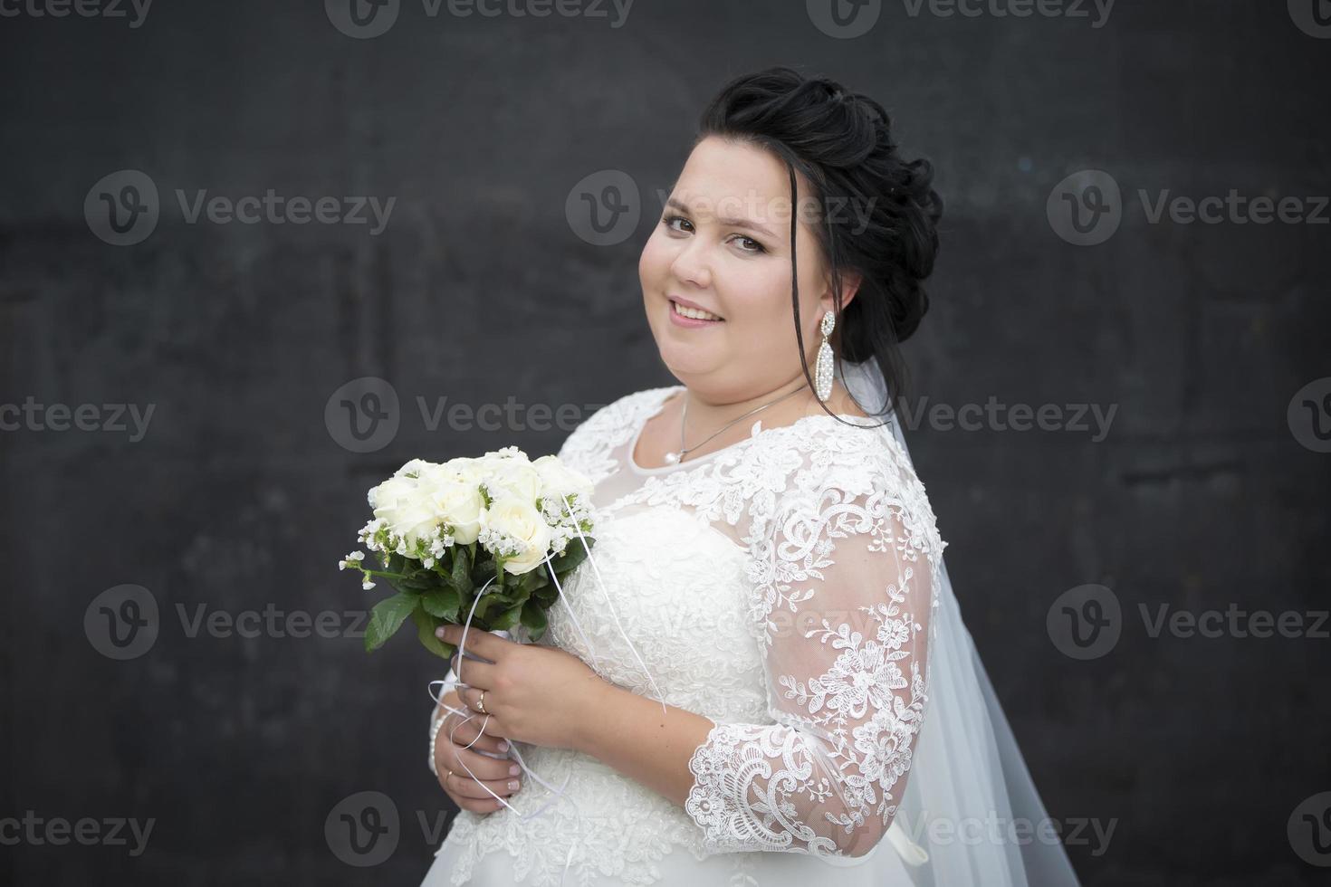 Beautiful fat bride posing with a bouquet of flowers on a dark background. photo