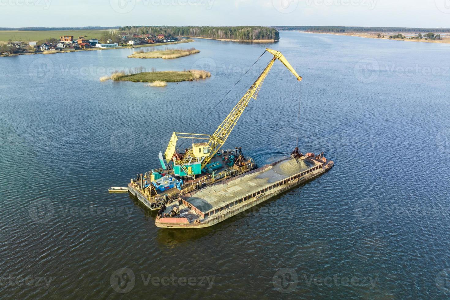aerial view on crane extracts minerals from bottom onto huge barge in middle of lake or sea photo