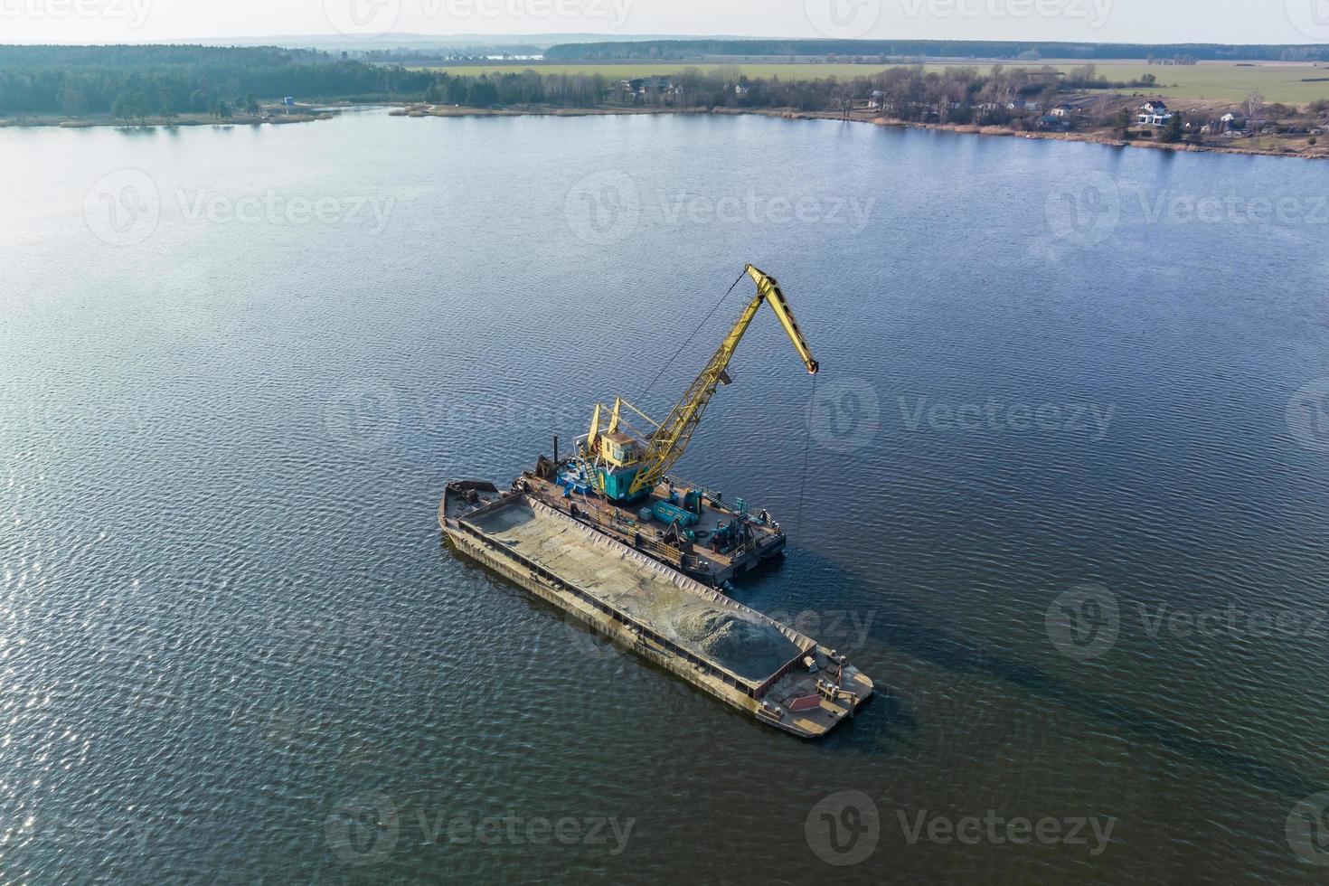 aerial view on crane extracts minerals from bottom onto huge barge in middle of lake or sea photo