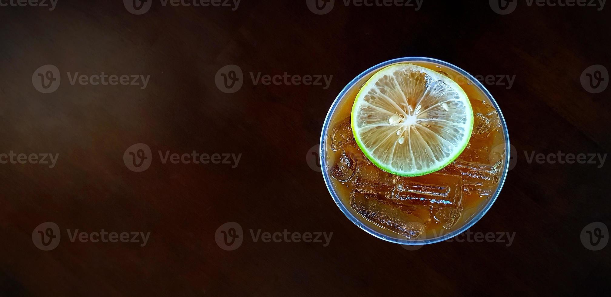 Top view of iced lemon tea on dark brown wooden background. Cup or plastic glass cool lime coffee on wood table with copy space. Refreshment drinking photo