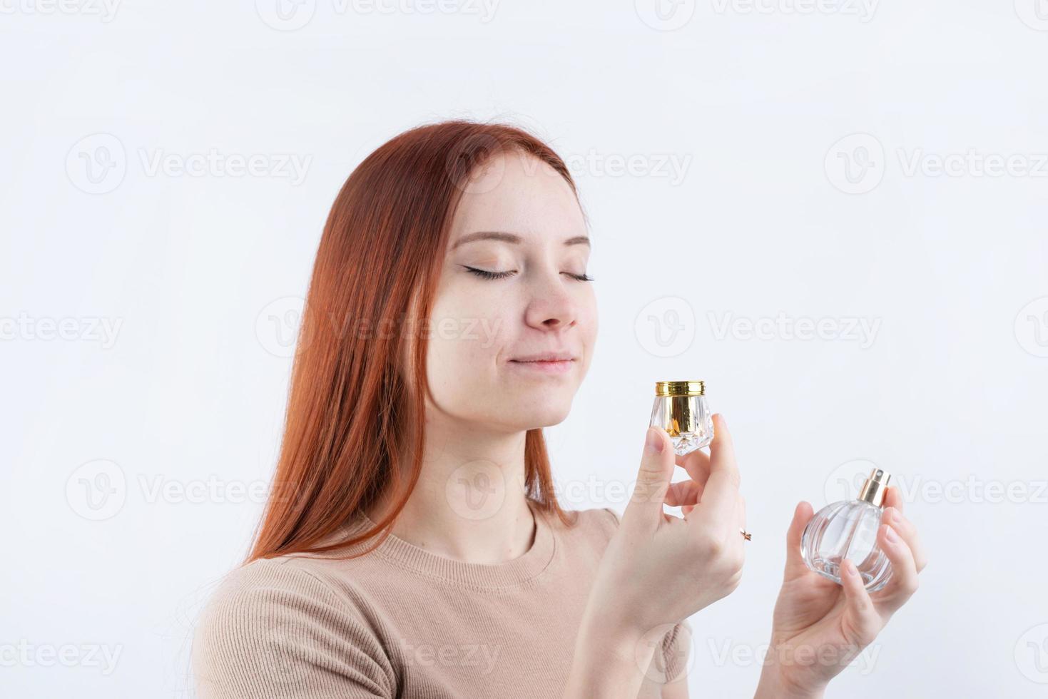 Happy young woman smelling perfume, holding glass bottle isolated on white background photo