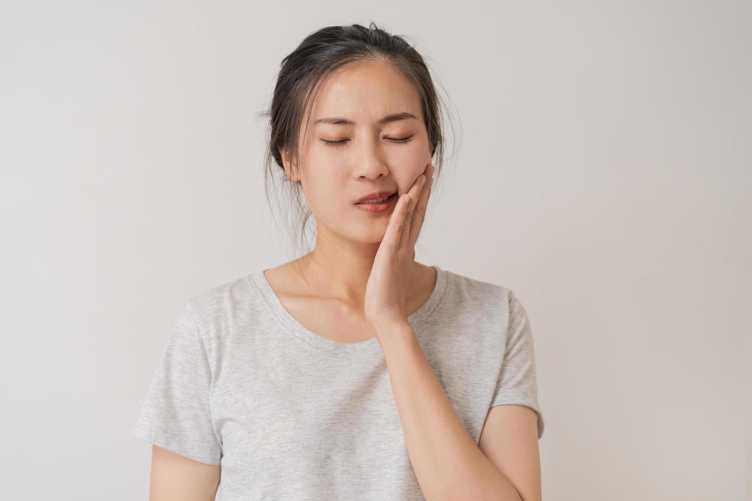 Closing eyes asian young woman touching cheek, face expression from toothache, tooth decay or sensitivity, Having tooth or teeth problem or inflammation, suffering from health. Sensitive teeth people photo