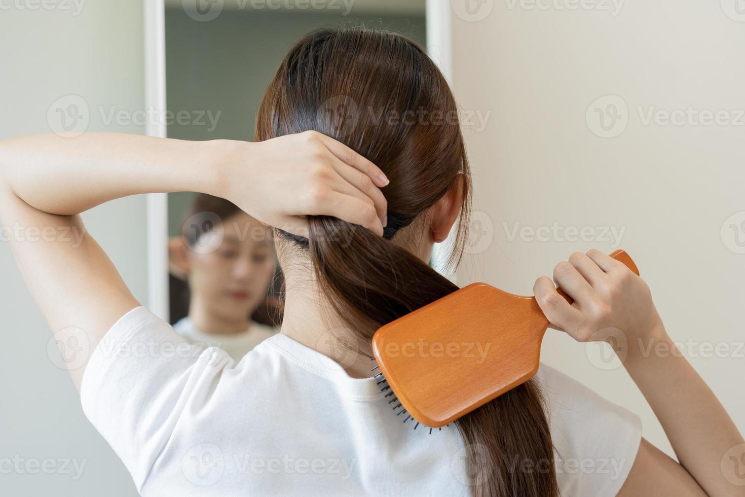 Health hair care, beauty makeup asian woman, girl holding hairbrush and brushing, combing her long straight hair looking at reflection in mirror in morning routine after salon treatment, hairstyle. photo