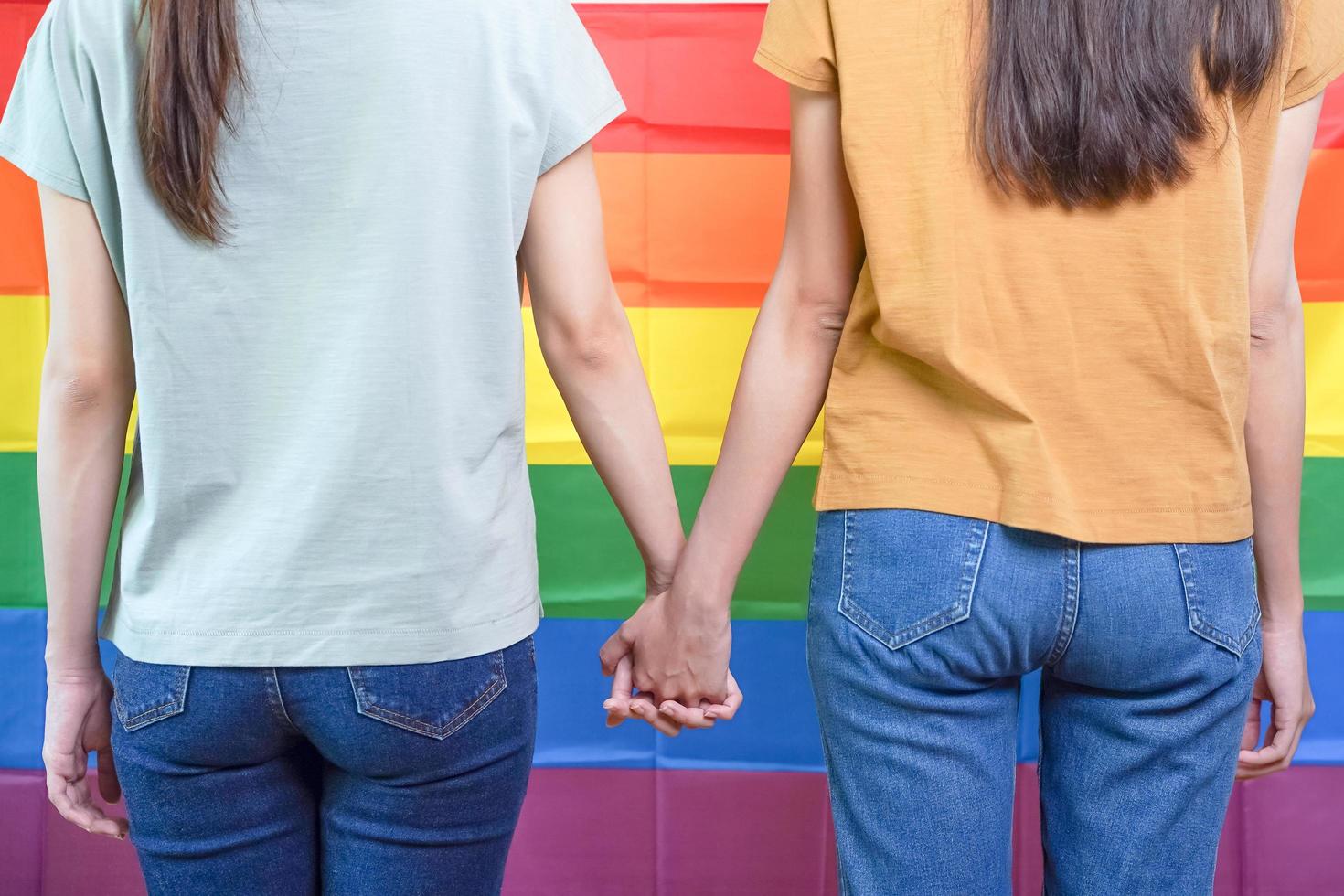 contento lesbiana, hermosa asiático joven dos mujer, niña gay o lesbianas, lgbtq Pareja amor momento gasto bueno tiempo, estar juntos participación manos en frente de orgullo arco iris bandera símbolo en aislado antecedentes foto