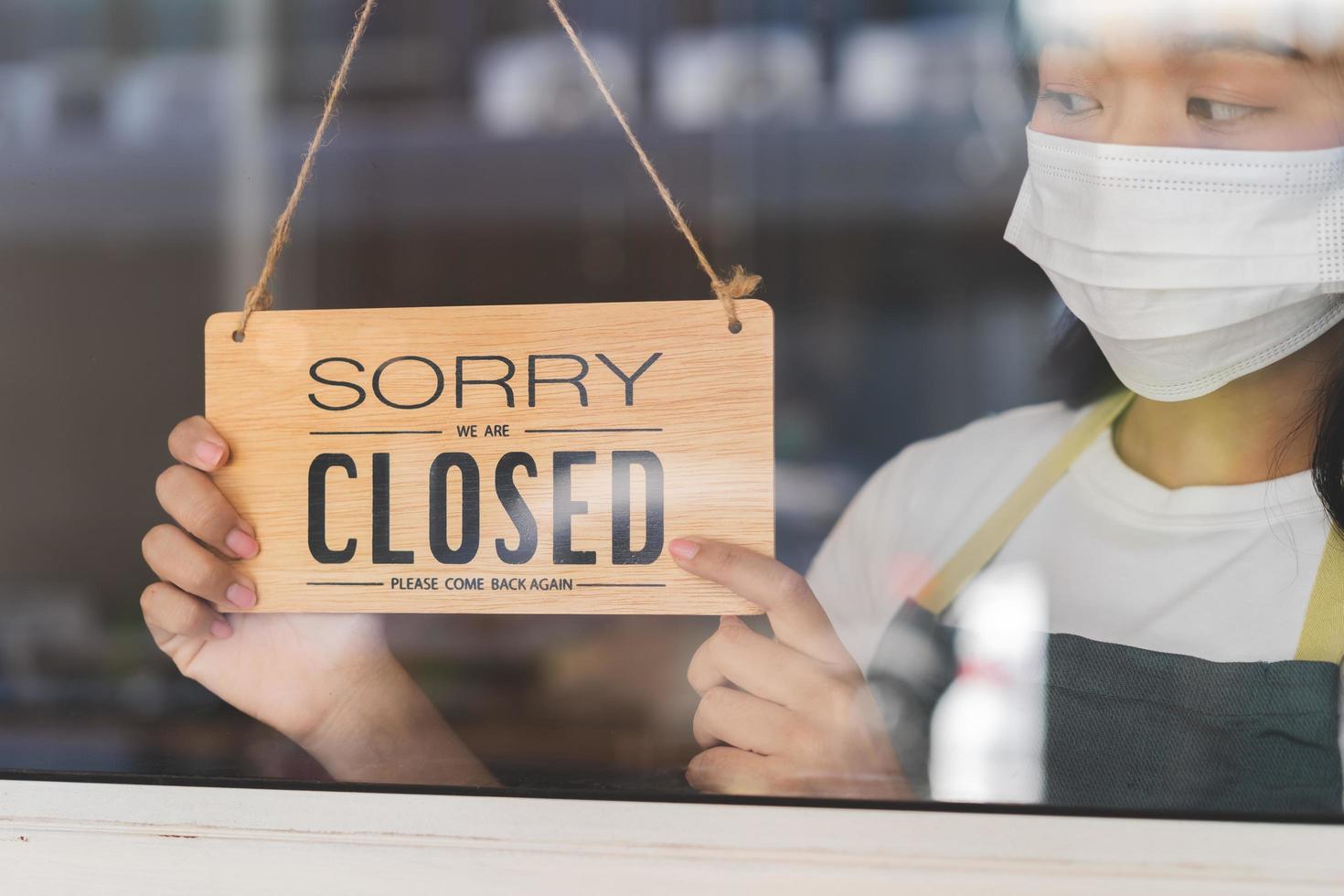 Asian young owner retail,coffee shop woman turning sign board to closed with wearing face mask,protection to pandemic of coronavirus.Close store,restaurant or pub due to lockdown, quarantine of covid. photo