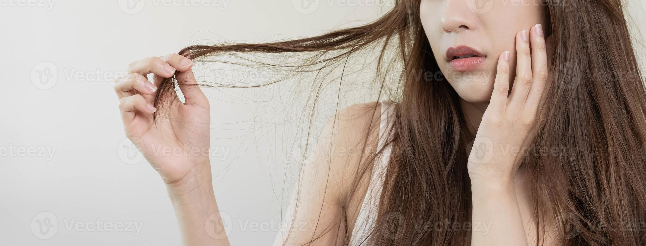Damaged Hair, frustrated asian young woman, girl hand in holding splitting ends, messy unbrushed dry hair with face shock, long disheveled hair, health care of beauty. Portrait isolated on background. photo