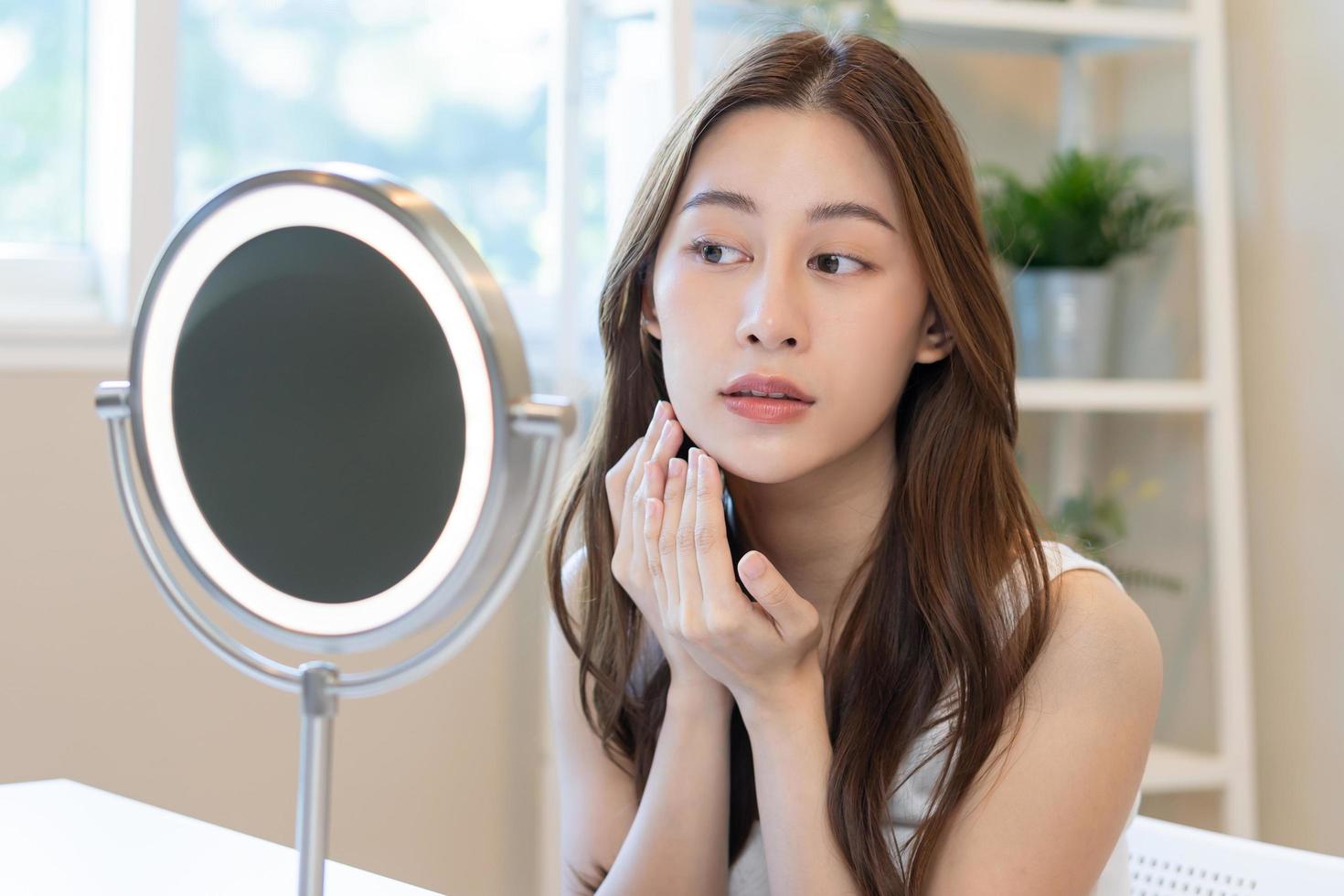 Fresh, nice healthy skin, beautiful of asian young woman, girl looking at mirror, touching her face with before make up cosmetic routine at home. Female look with natural fashion style, Facial Beauty. photo