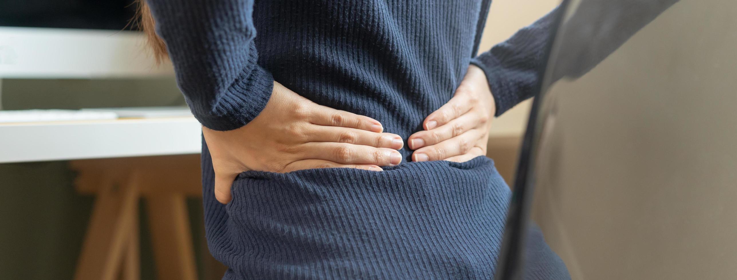 cuerpo músculos rígido problema, asiático joven atractivo mujer, niña dolor con espalda dolor dolor desde computadora trabajar, participación masajear frotamiento, herir o dolorido mientras sentado en silla a hogar. cuidado de la salud gente. foto