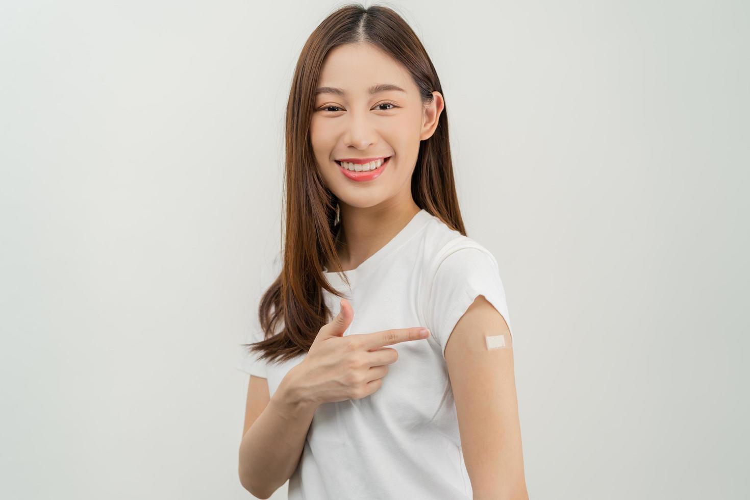 Portrait of pretty, beautiful asian young, teenage attractive after getting, receive anti virus vaccine covid-19. Showing arm on white bandage isolated on white background, copy space. photo