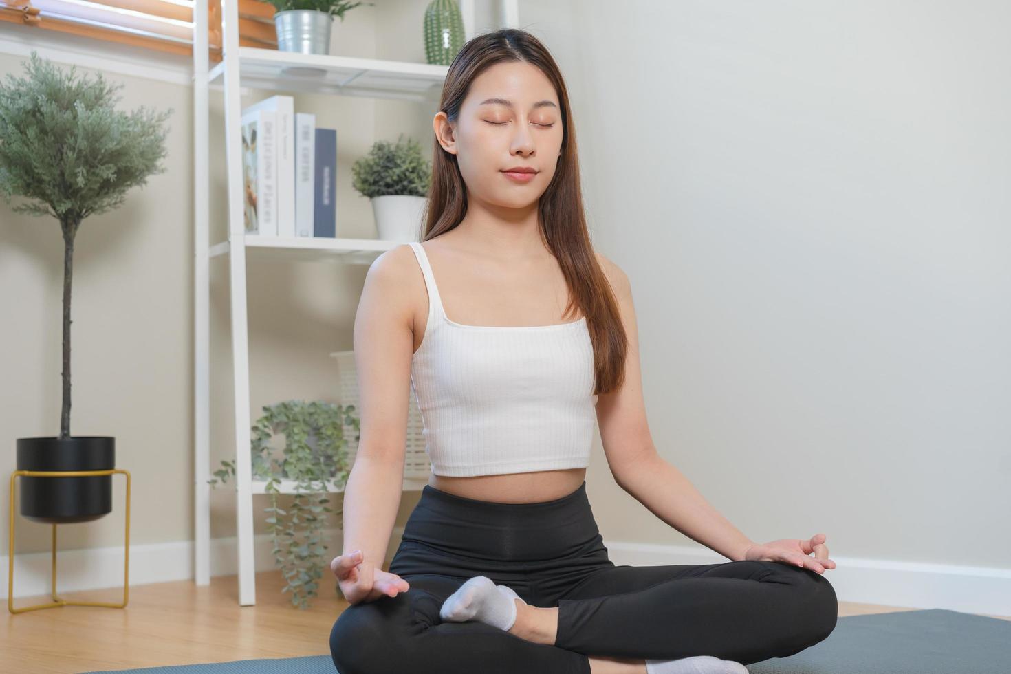 Workout, calm asian young woman, girl hand in calm pose sitting practice meditating in lotus position on mat at home, meditation, exercise for wellbeing, healthy care. Relaxation, happy leisure. photo