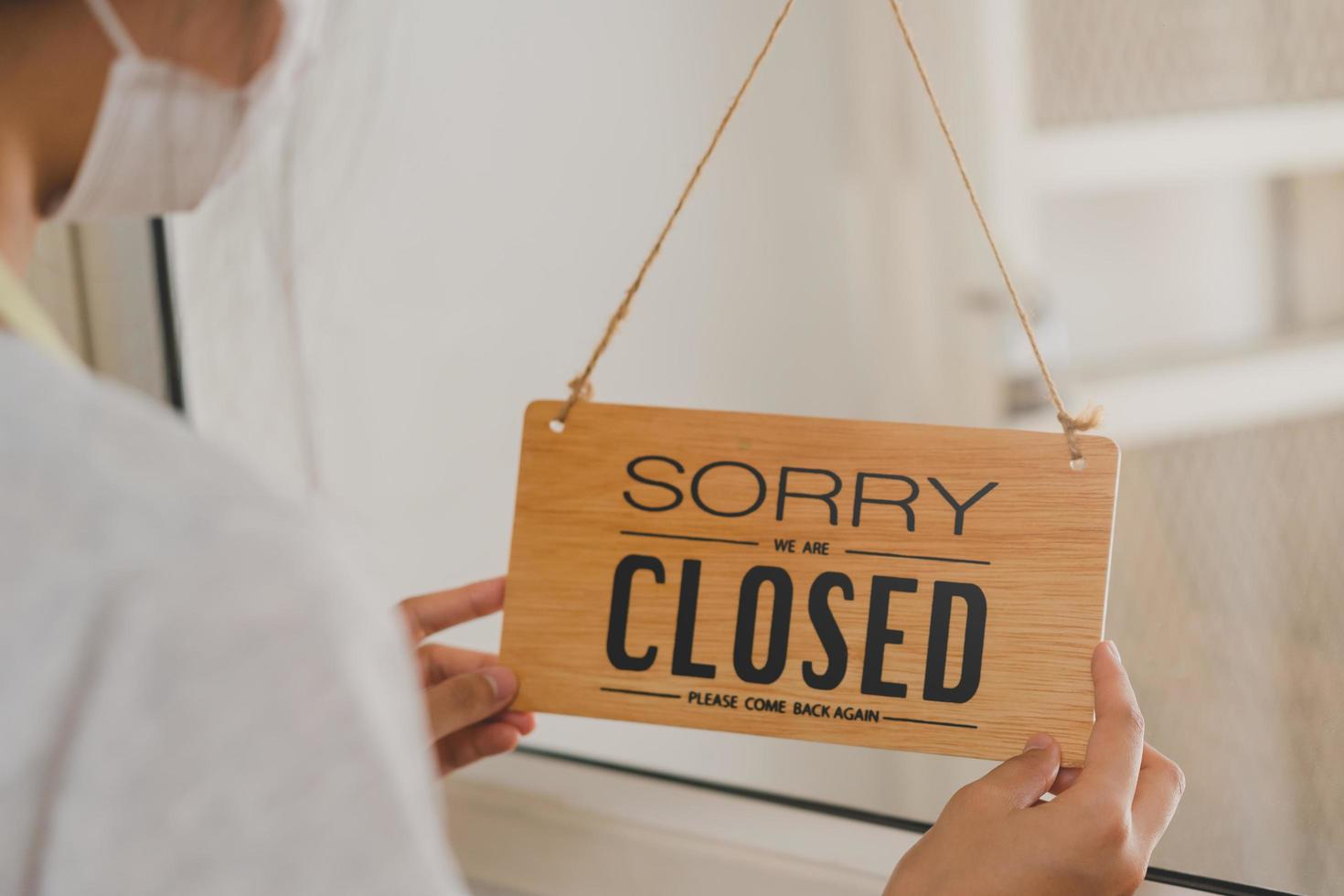 Asian young owner retail,coffee shop woman turning sign board to closed with wearing face mask,protection to pandemic of coronavirus.Close store,restaurant or pub due to lockdown, quarantine of covid. photo