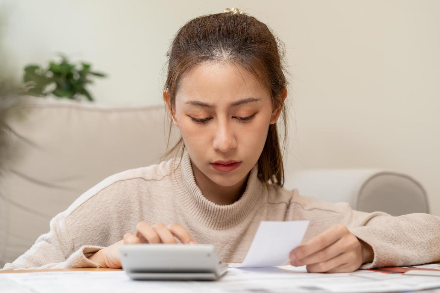 financiero deber asiático joven mujer, niña sentado sufrir, estresado y confuso por calcular gastos desde factura o factura, tener No dinero a pagar, hipoteca o préstamo. deuda, bancarrota o bancarrota concepto. foto